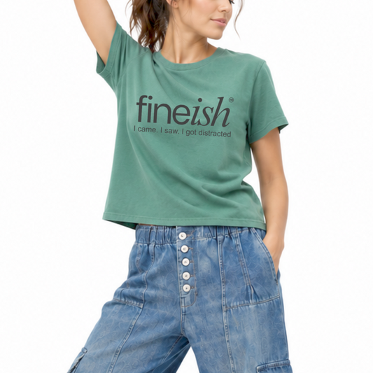 Woman wearing a washed pine garment-dyed FINEish T-shirt featuring the “I Came, I Saw, I Got Distracted” graphic.