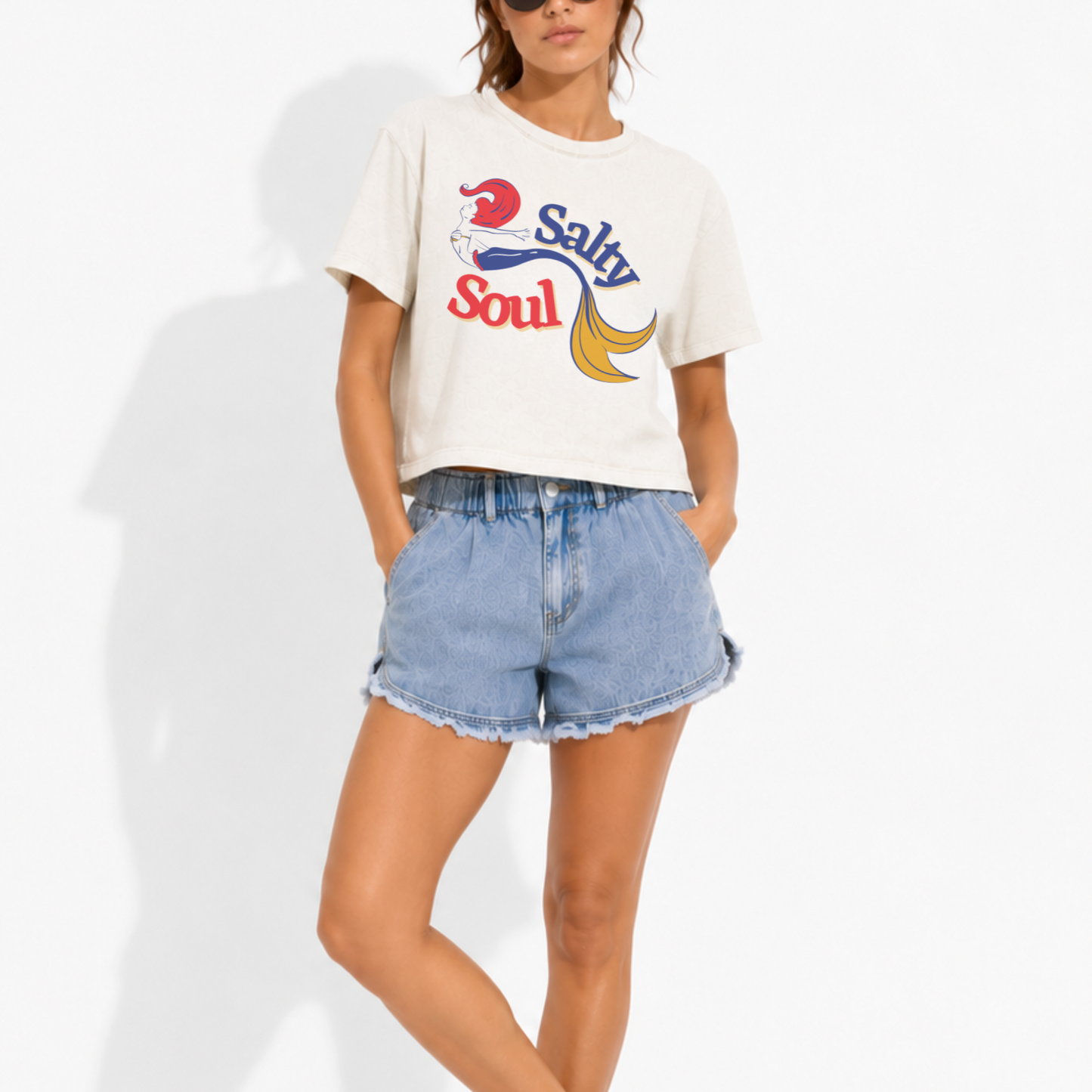 Woman wearing a heavyweight boxy crop tee featuring the phrase "Salty Soul" with an elegant mermaid graphic, creating a fun coastal-inspired summer look.